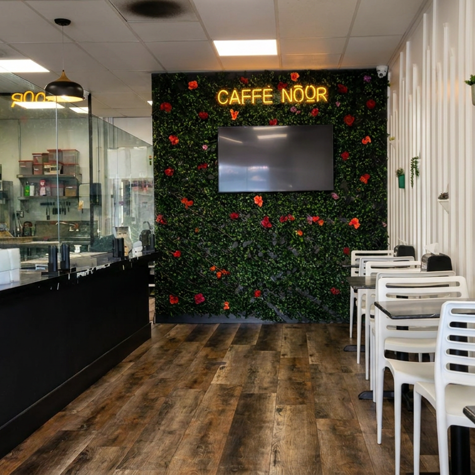 Modern Caffè Noor interior with black counter, white seating, floral green wall, neon sign, and wall-mounted television.