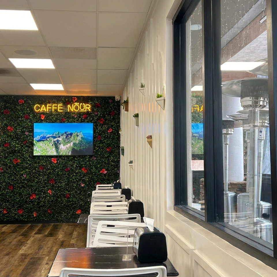 Caffe Noir café interior with a flower-covered wall, mountain video display, counter, seating, and outdoor patio heaters.