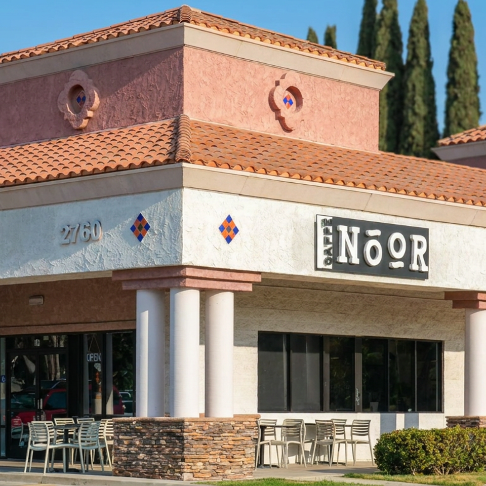 Exterior of Anor restaurant with terracotta roof, stucco walls, covered patio seating, columns, and tall cypress trees.